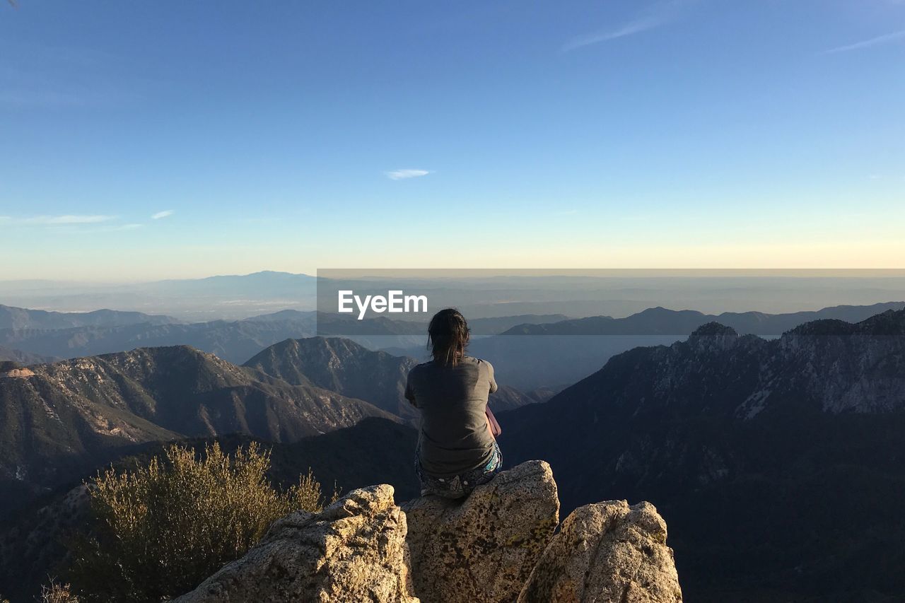 Rear view of young woman sitting on mountain against sky