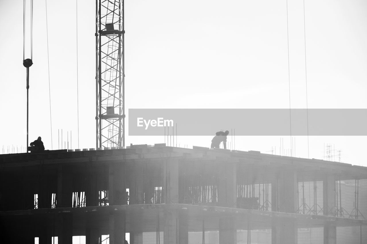 Silhouette man working at construction site against clear sky