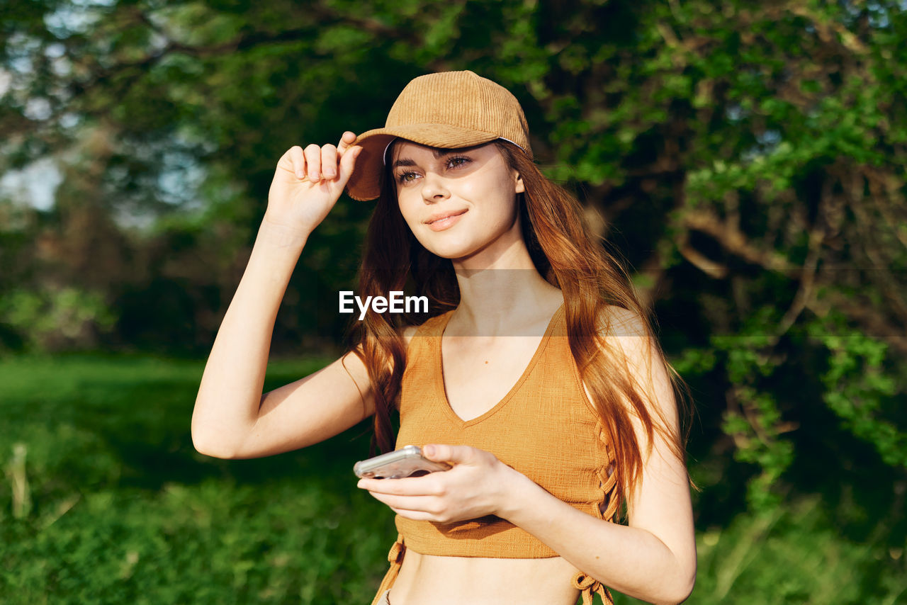 portrait of young woman wearing hat standing against plants