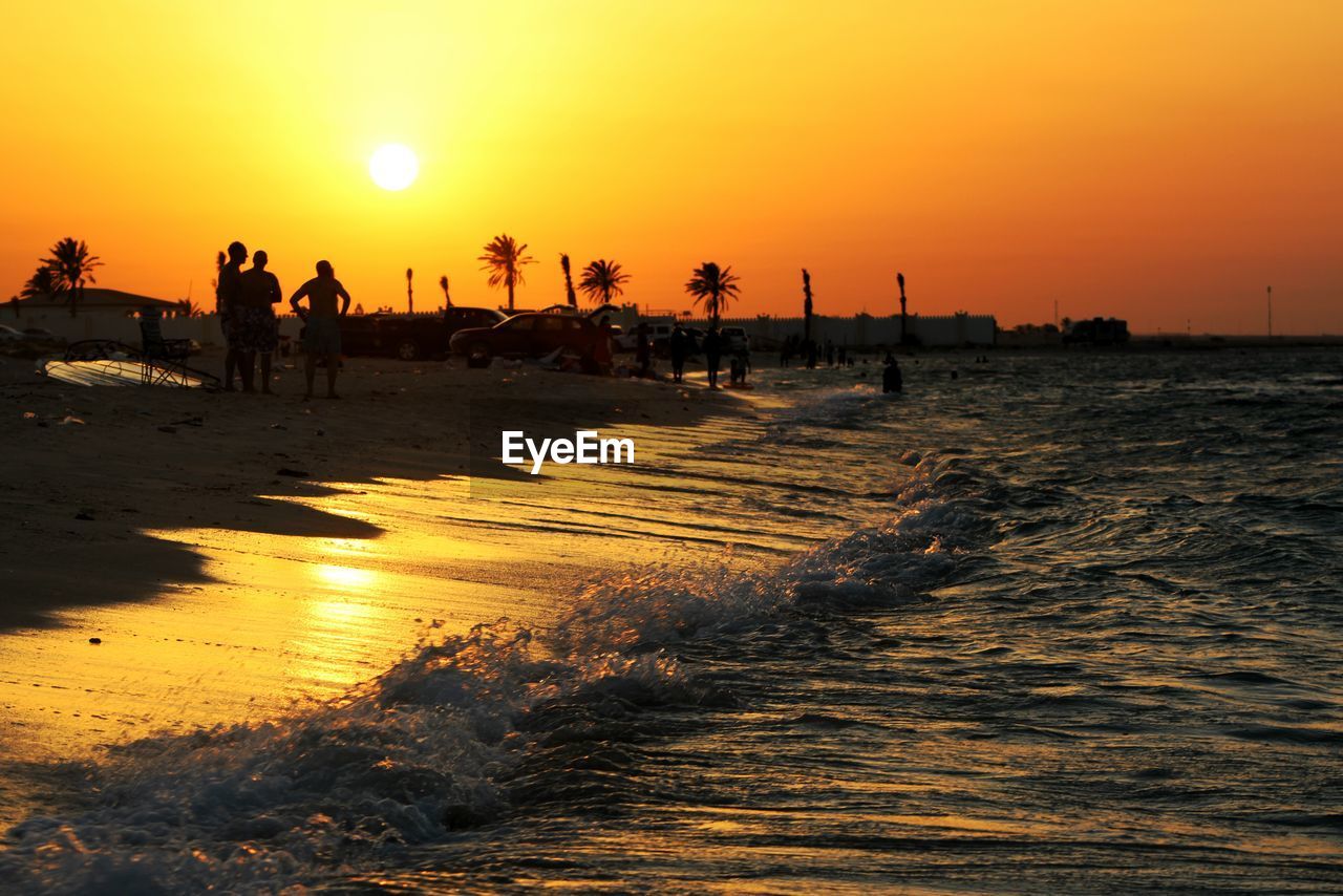 Silhouette people standing at beach against sky during sunset