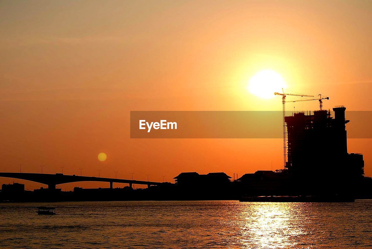 SILHOUETTE CRANES BY SEA AGAINST ORANGE SKY