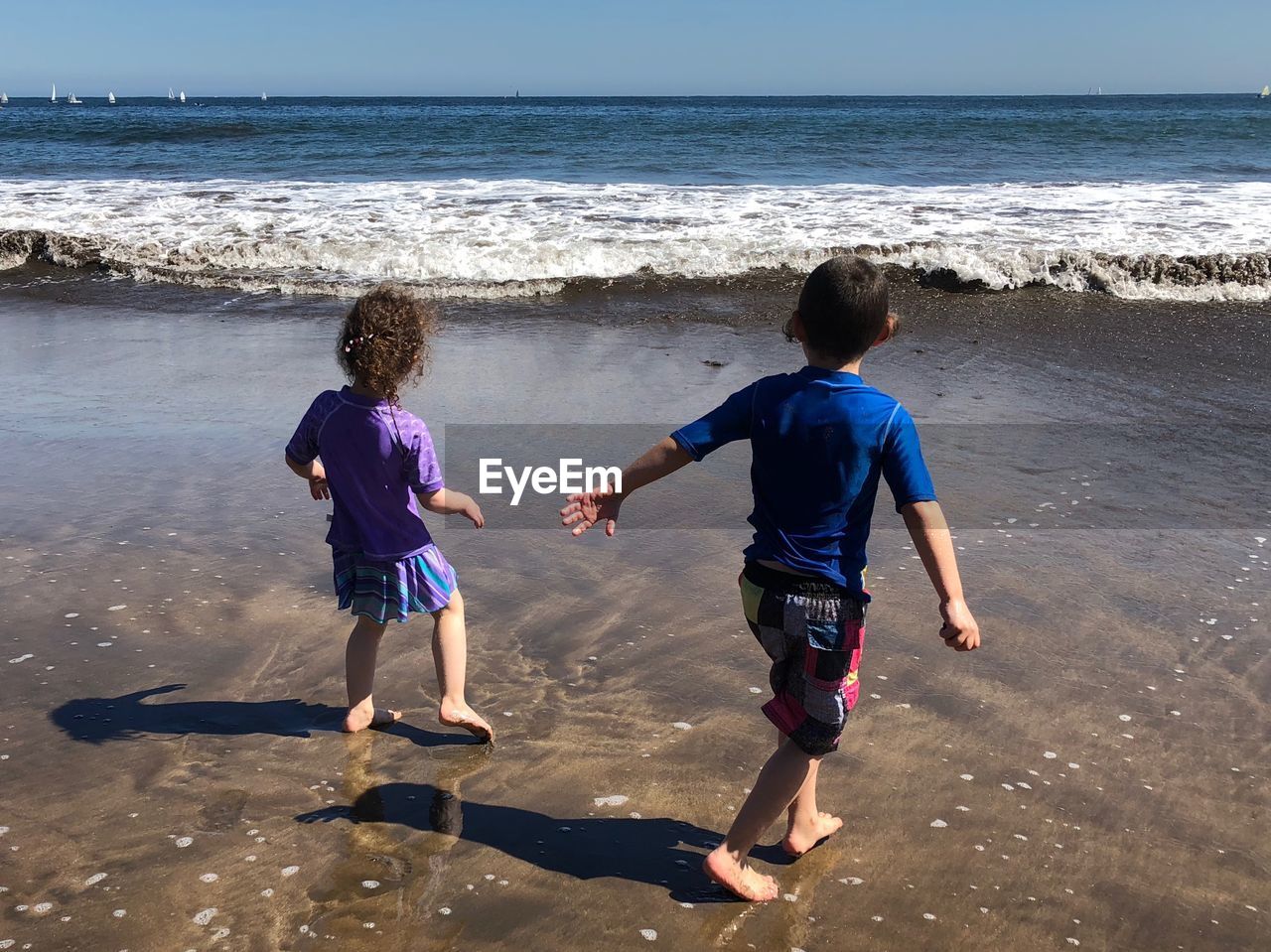 REAR VIEW OF FRIENDS ON SHORE AT BEACH