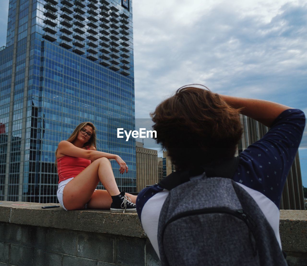 YOUNG WOMAN SITTING AGAINST OFFICE BUILDING