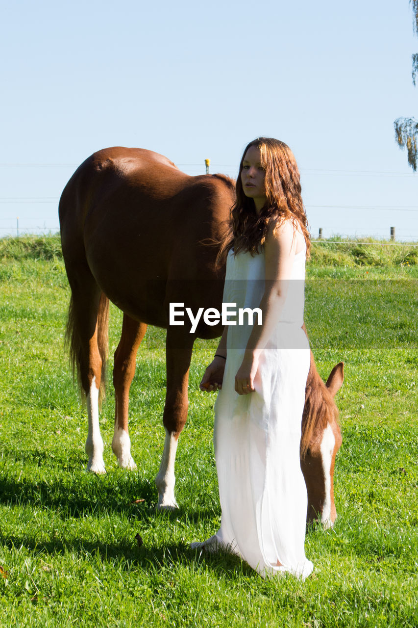 Side view of young woman with horse walking on grassy field against clear sky
