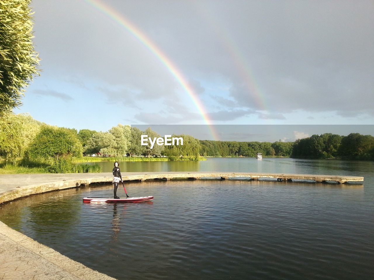 Woman standing on paddleboard in river against double rainbow