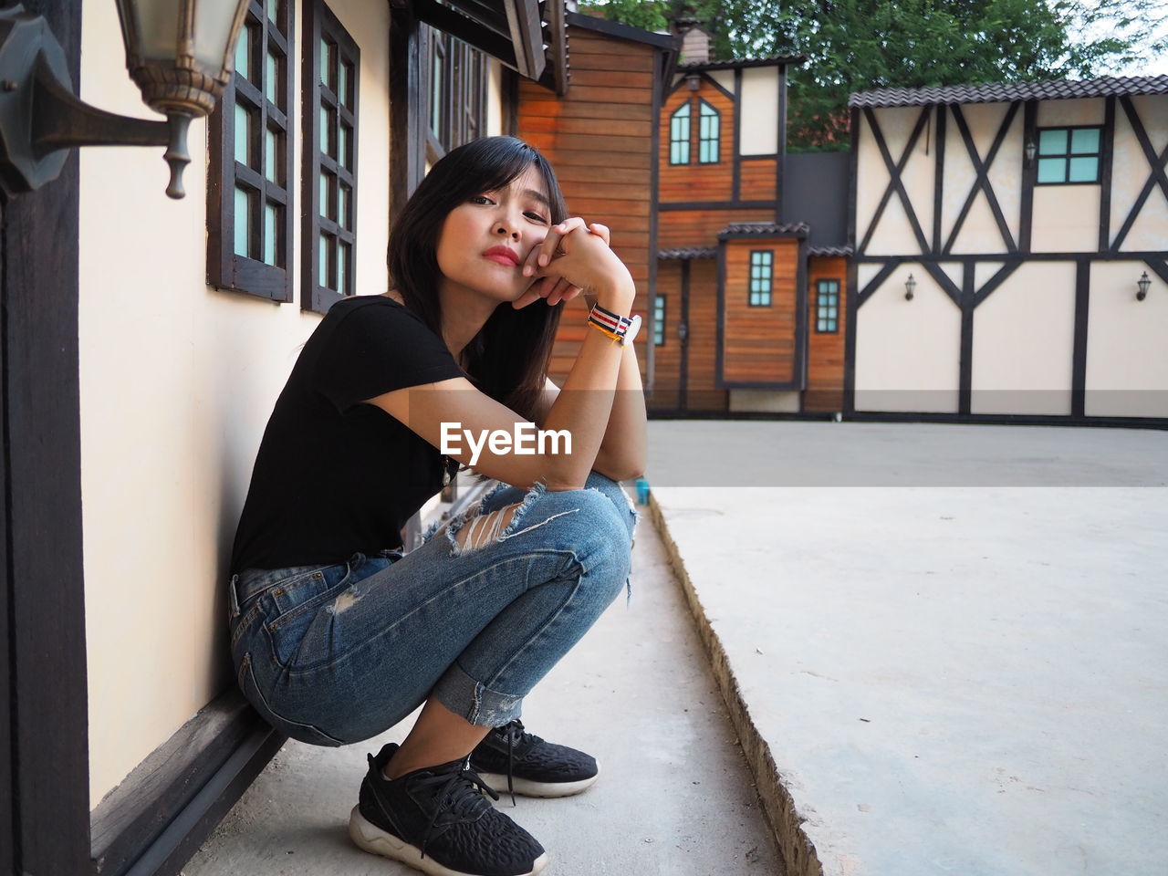 Side view portrait of young woman crouching against houses