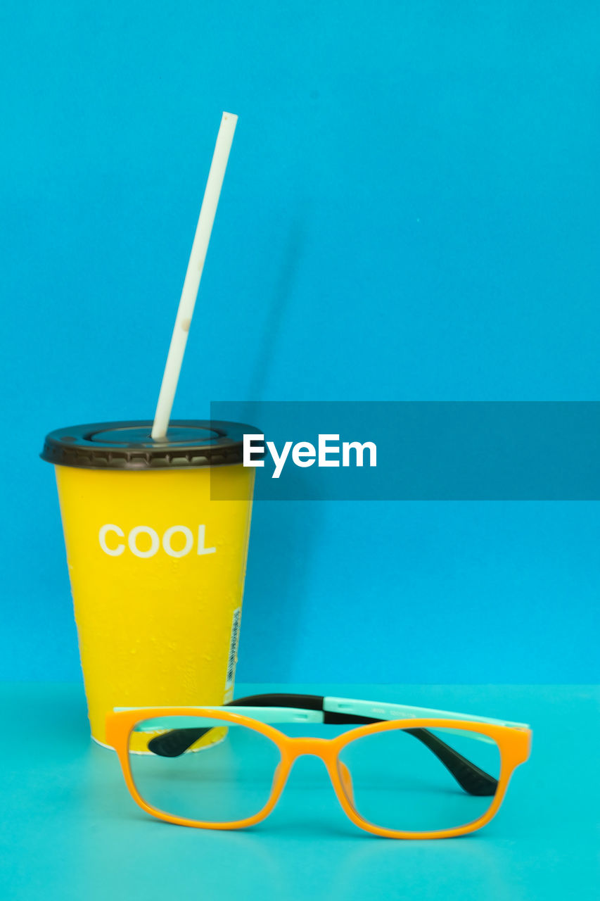 Close-up of eyeglasses and drink against blue background