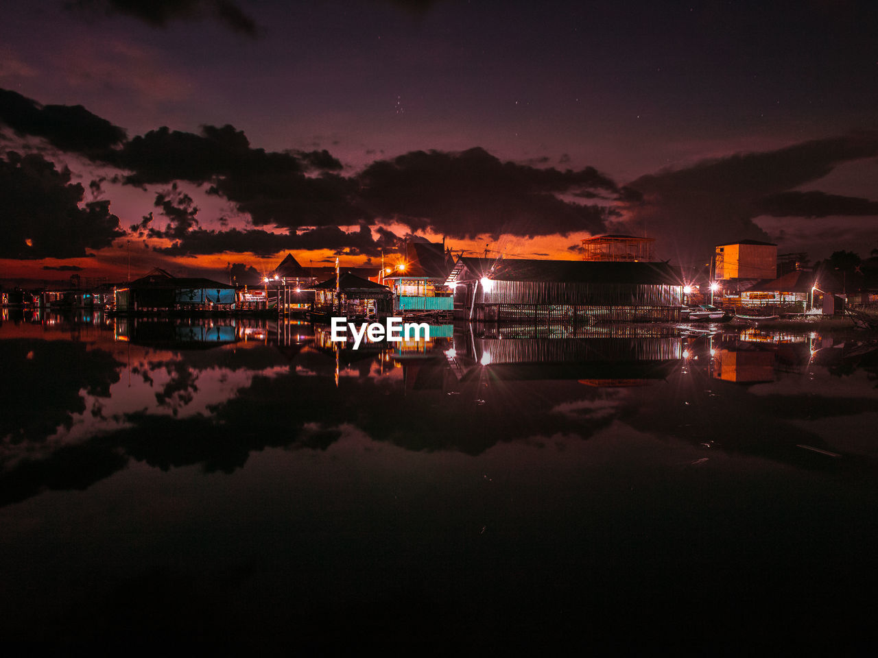 Illuminated buildings by lake against sky at night