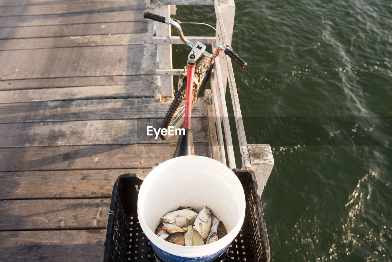 High angle view of fish in bucket on pier by sea