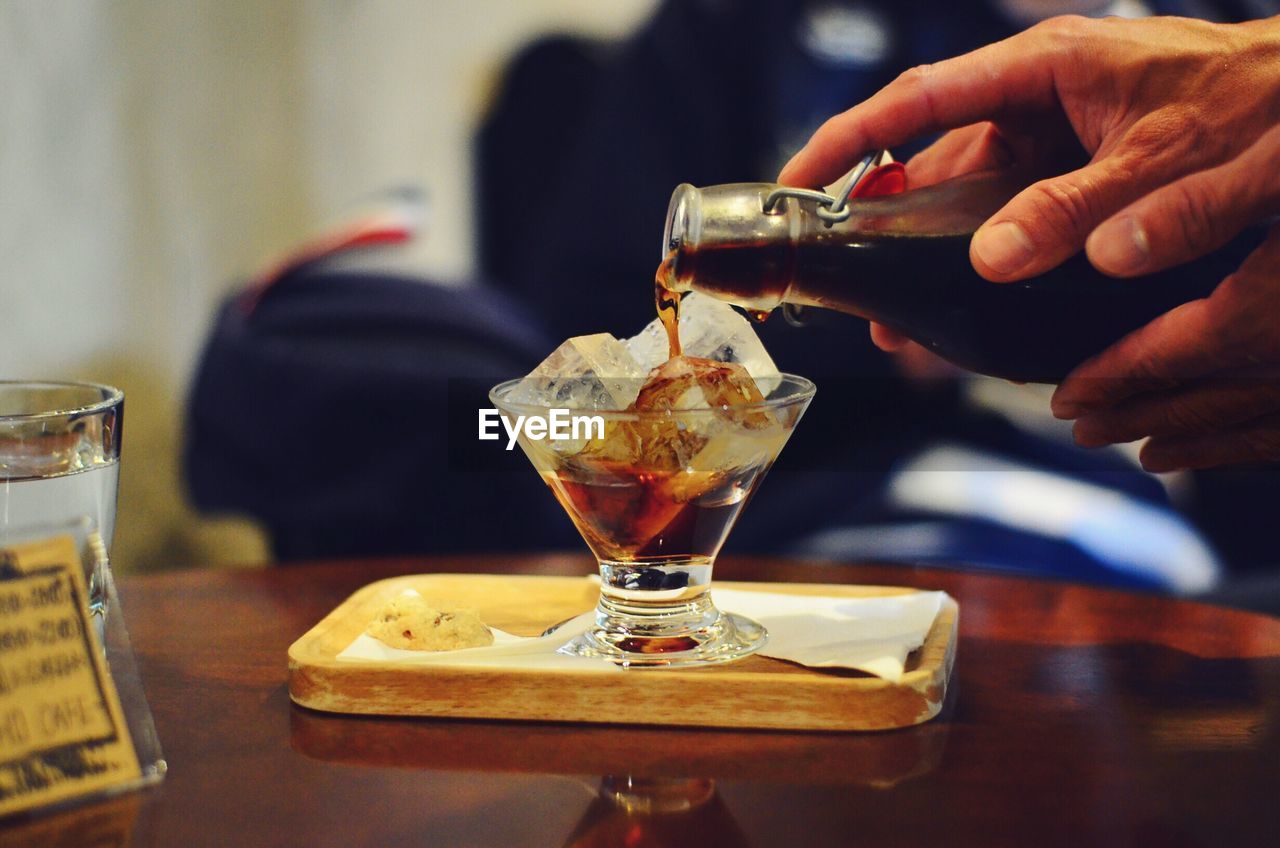 Cropped hand pouring alcohol in glass on table