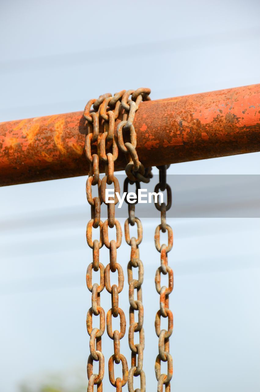 Close-up of rusty chain hanging against sky