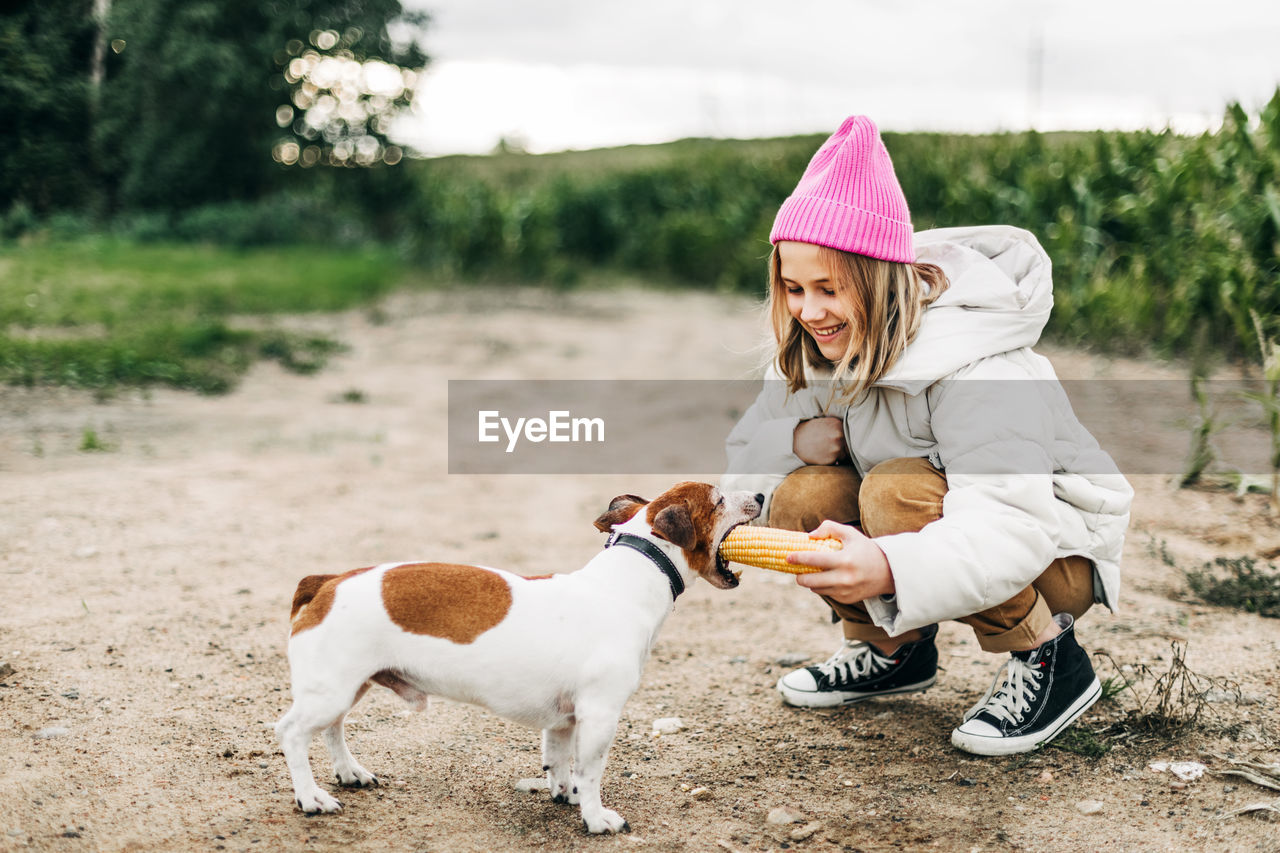 Happy teenage girl hugging and feeding her dog jack russell terrier in a field 