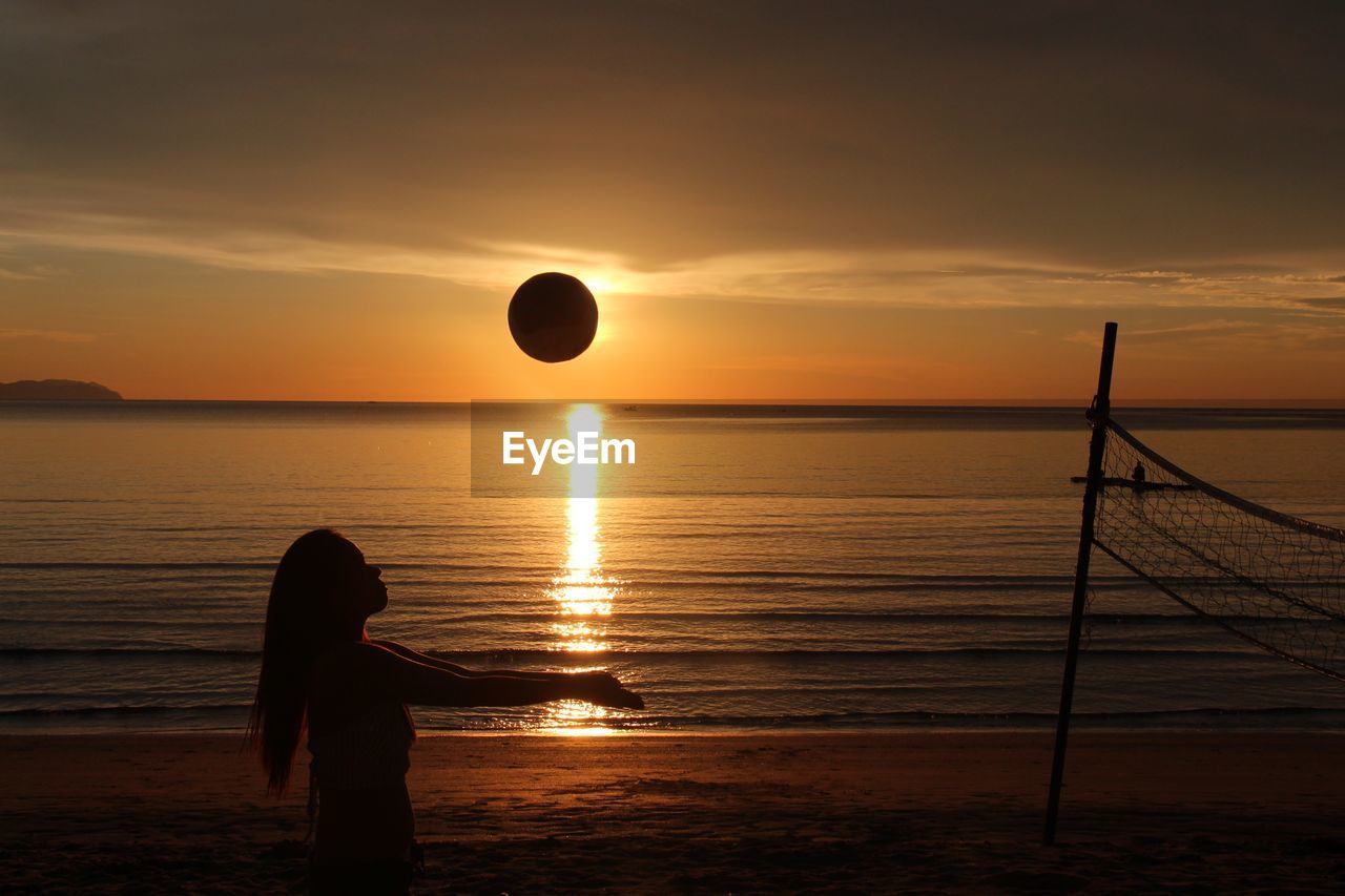 Silhouette woman playing volleyball at beach against sky during sunset