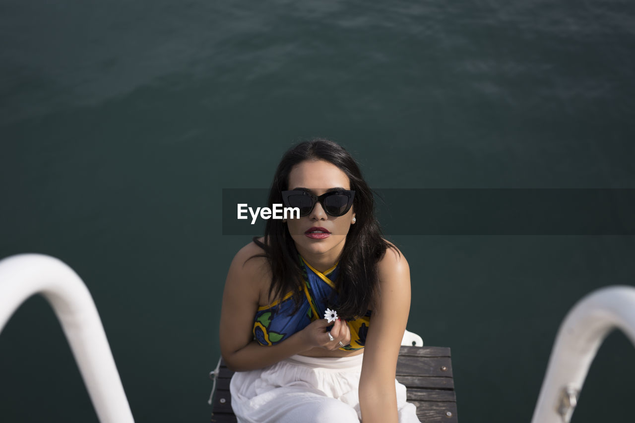 From above of a young woman in casual clothes and sunglasses looking at the camera