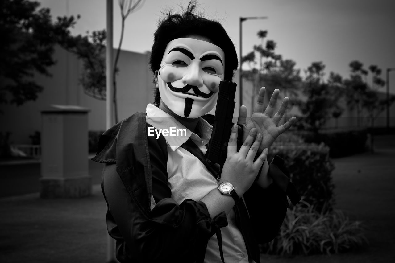 Portrait of a person wearing a mask holding up a fake gun while clapping