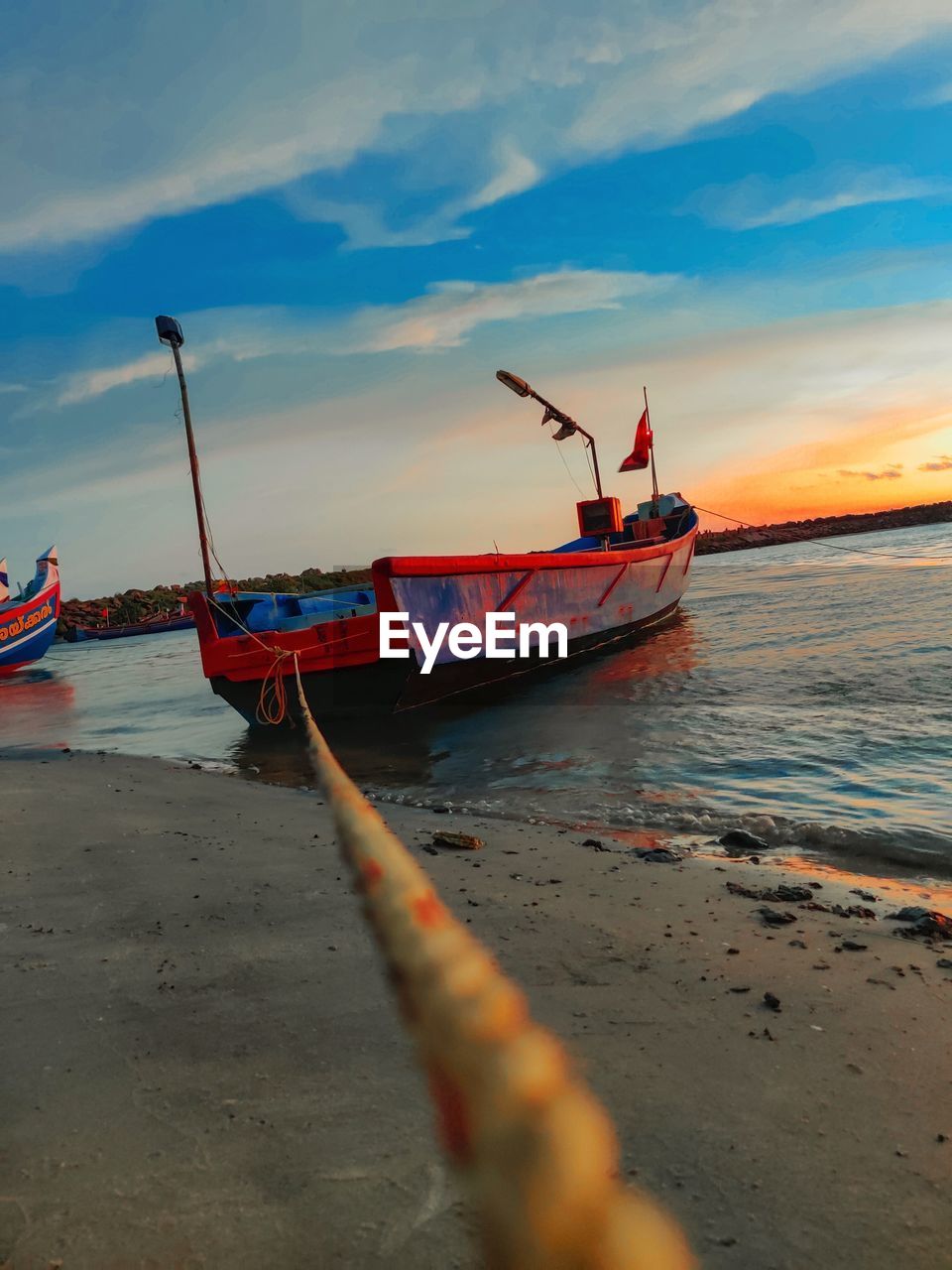 FISHING BOAT MOORED ON BEACH AGAINST SKY DURING SUNSET