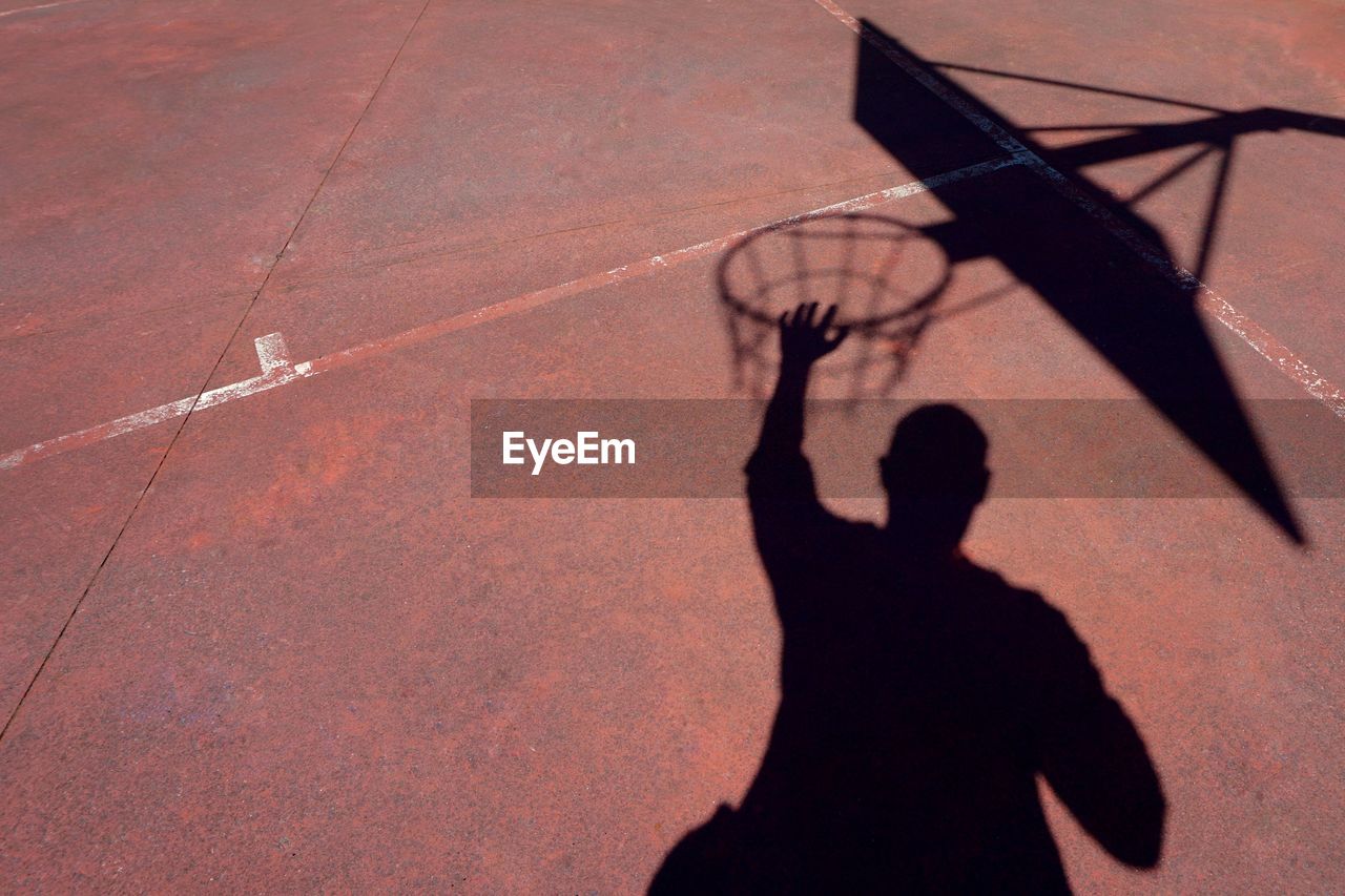 Shadow of man playing basketball on footpath