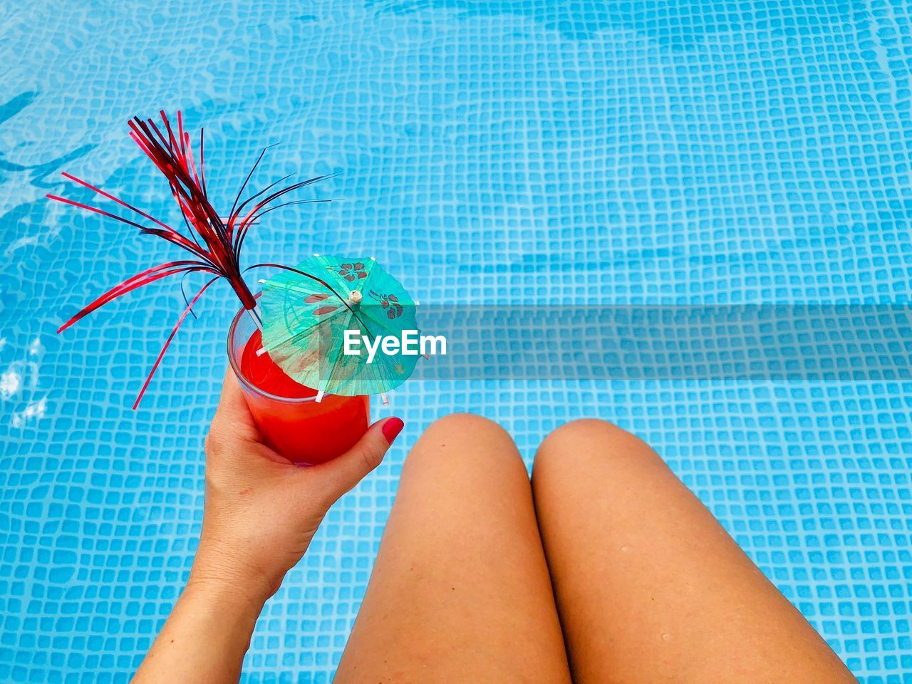 Midsection of woman holding drink while sitting by swimming pool