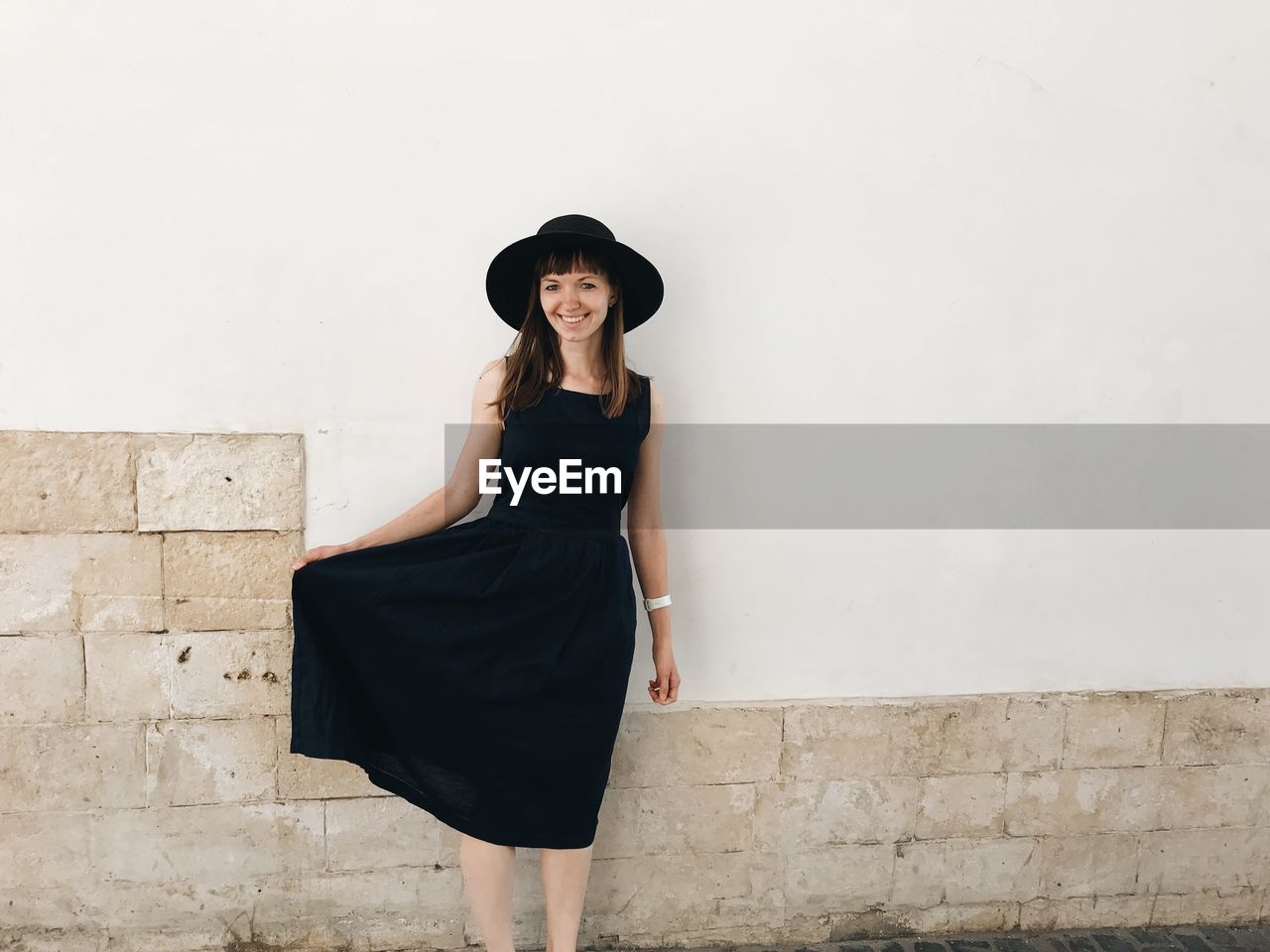 Portrait of smiling young woman standing against wall