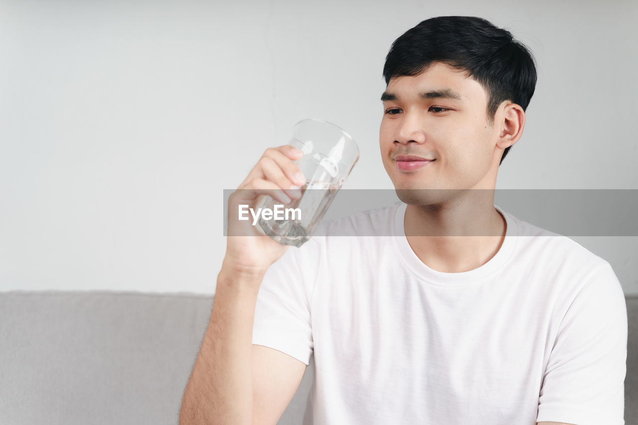 PORTRAIT OF YOUNG MAN DRINKING GLASS ON WHITE