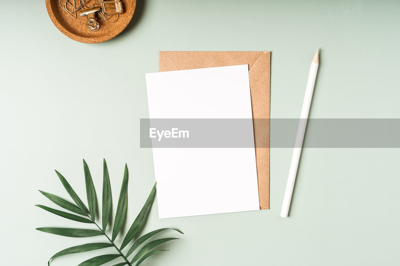 Flat lay craft paper envelope with white blank paper note mockup on green background, top view