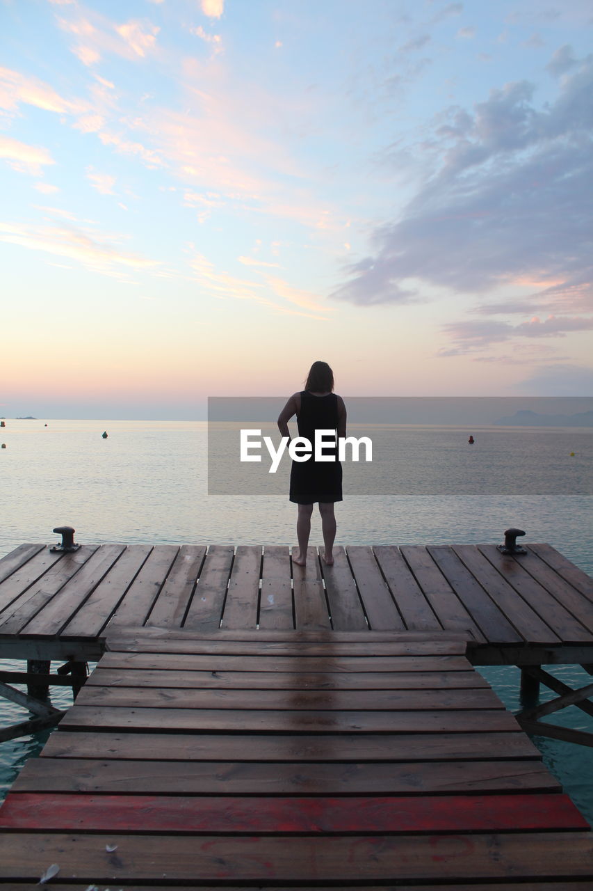 REAR VIEW OF WOMAN STANDING BY SEA AGAINST SKY