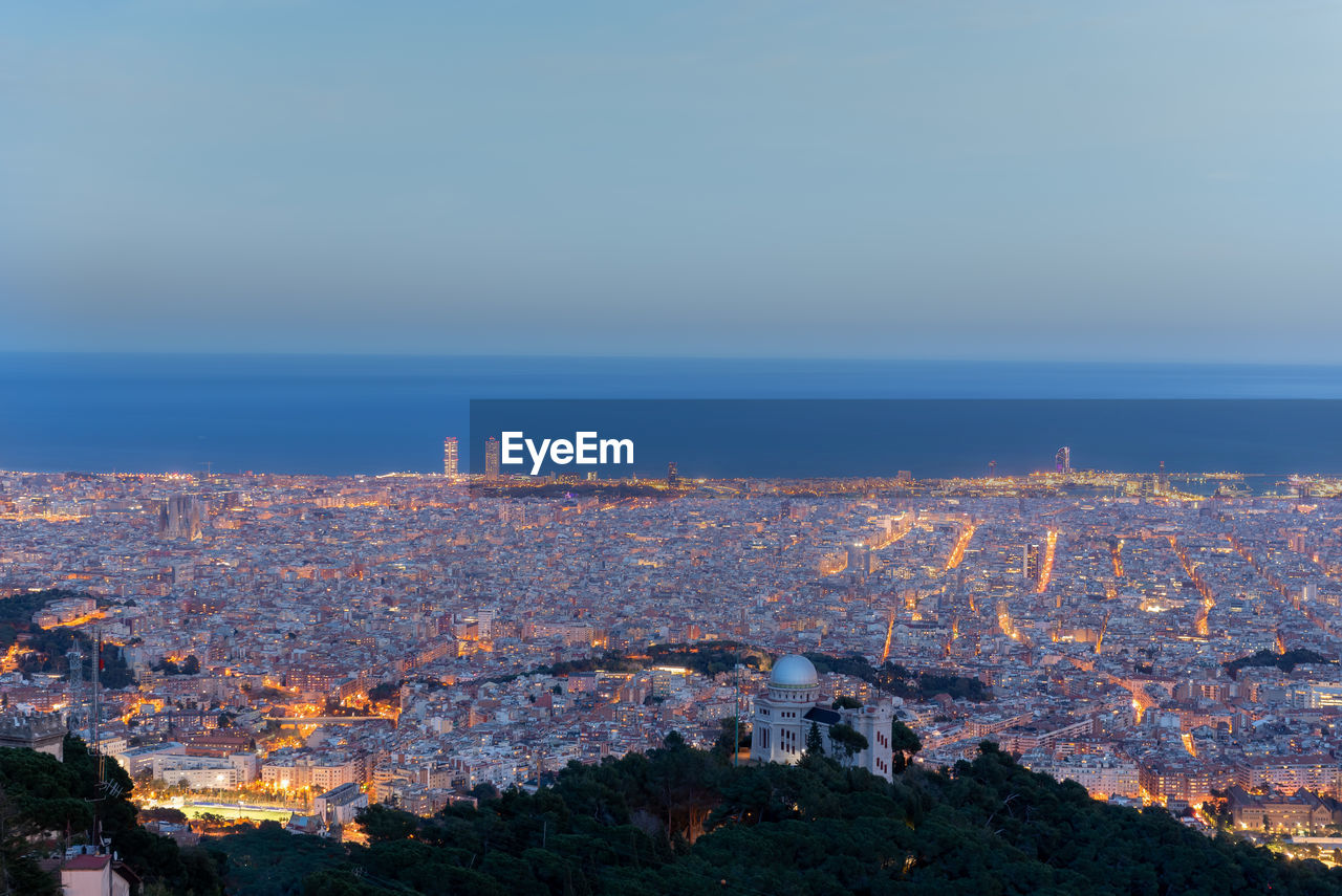 HIGH ANGLE VIEW OF ILLUMINATED BUILDINGS IN CITY AGAINST SKY