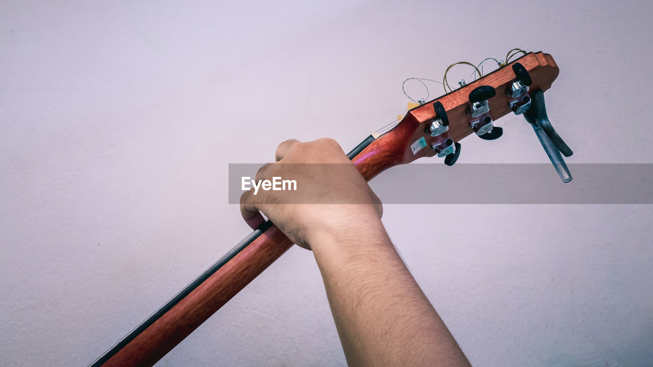 Cropped hand of man holding musical equipment against wall