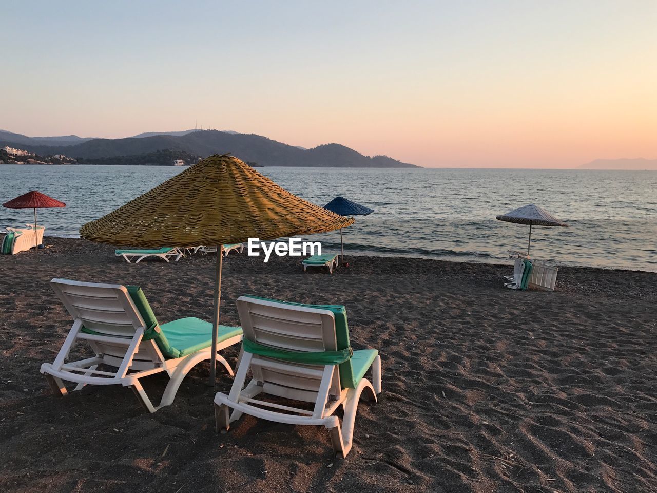 DECK CHAIRS ON BEACH AGAINST SKY DURING SUNSET