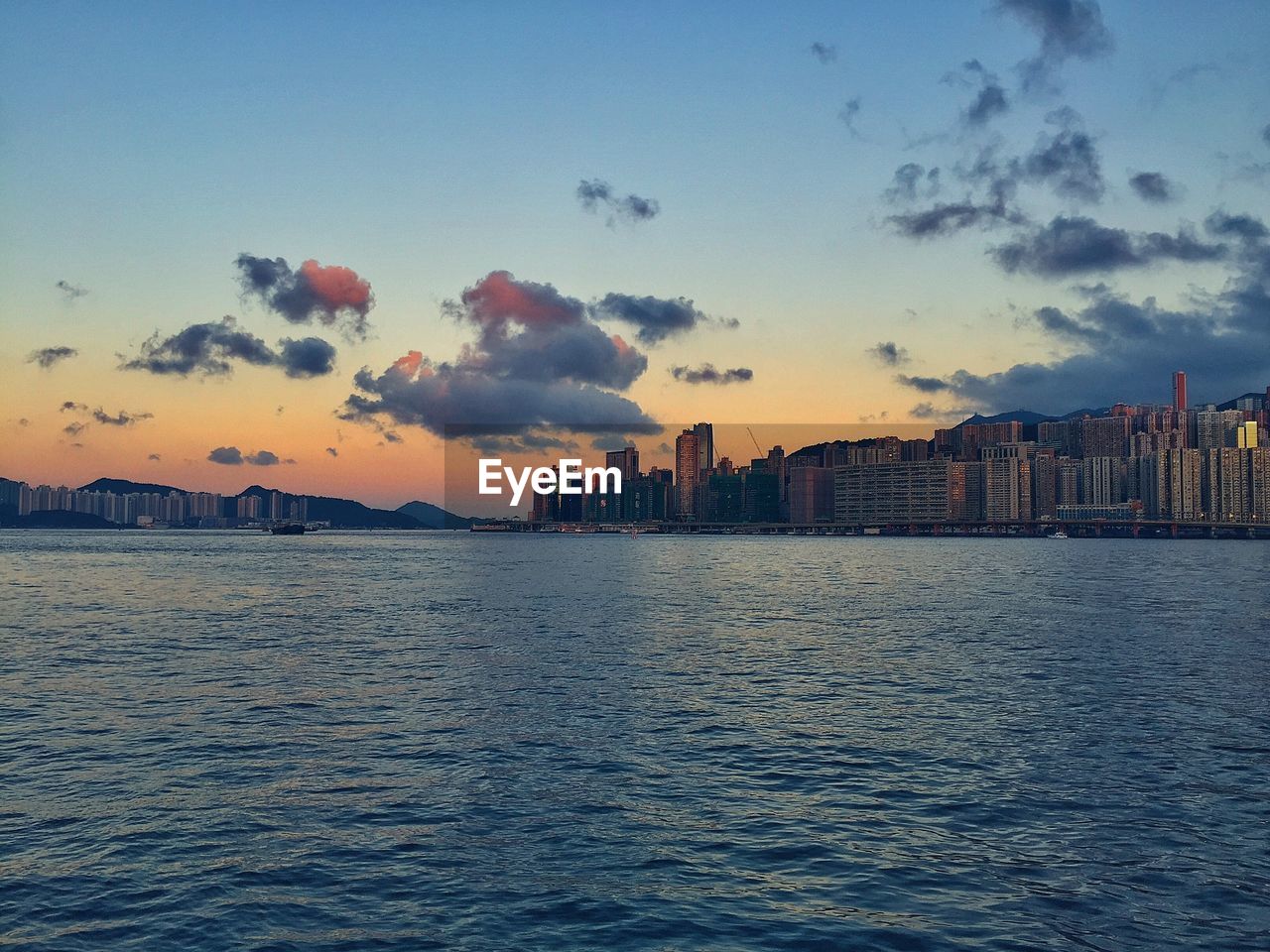 Scenic view of sea with cityscape in background against sky during sunset