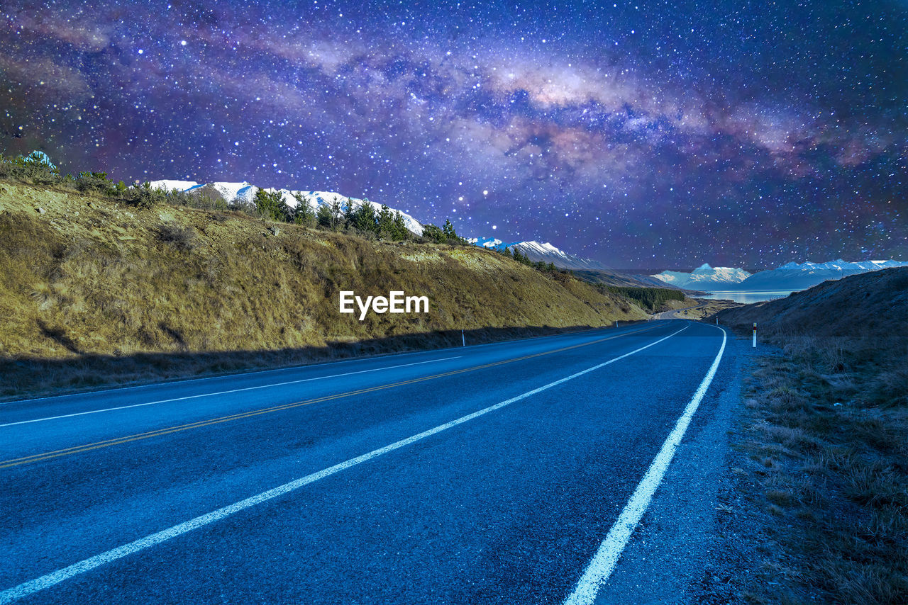 ROAD AMIDST LANDSCAPE AGAINST STAR FIELD AT NIGHT