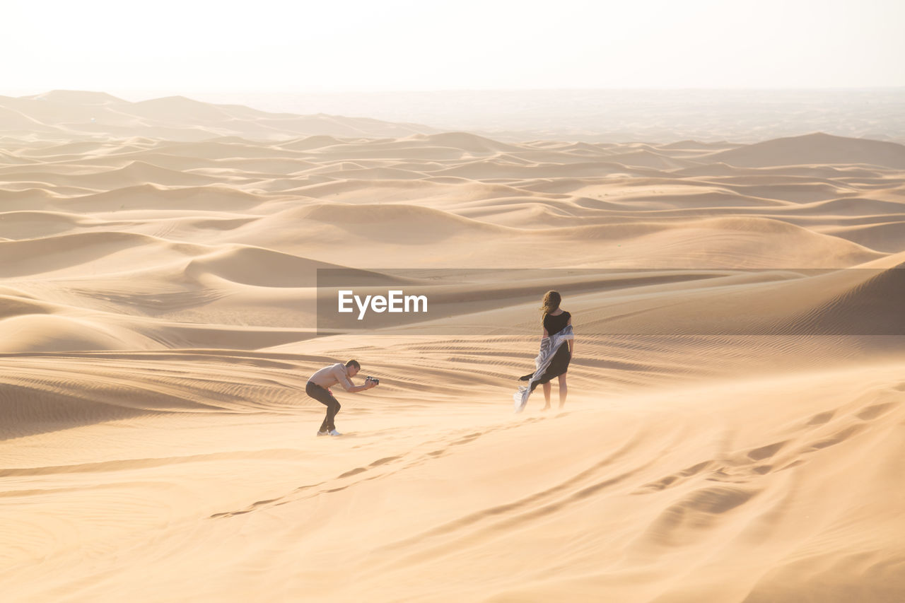 Man photographing woman standing at desert