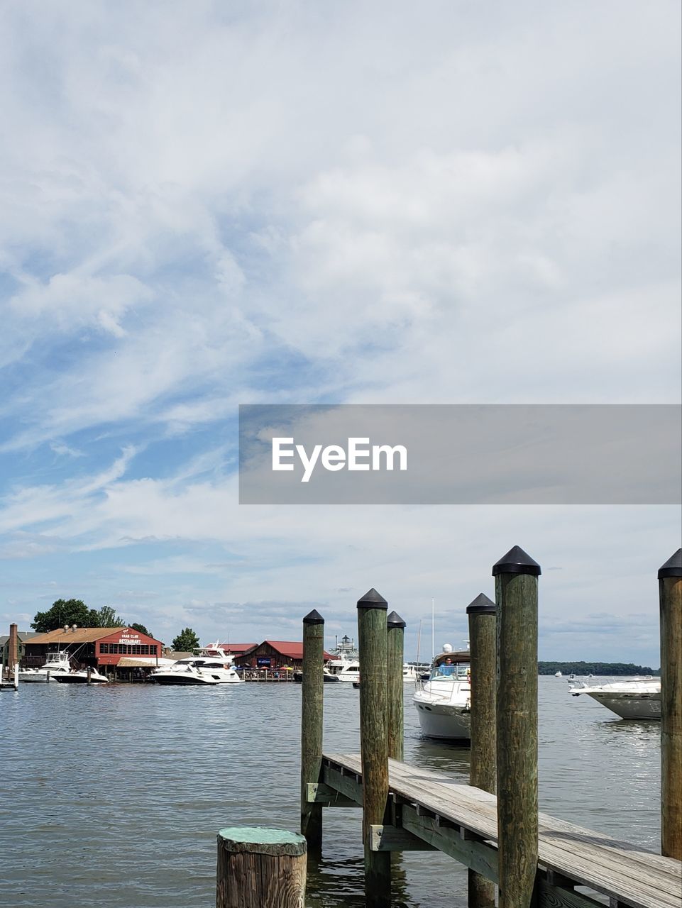 WOODEN POSTS ON PIER OVER SEA AGAINST SKY