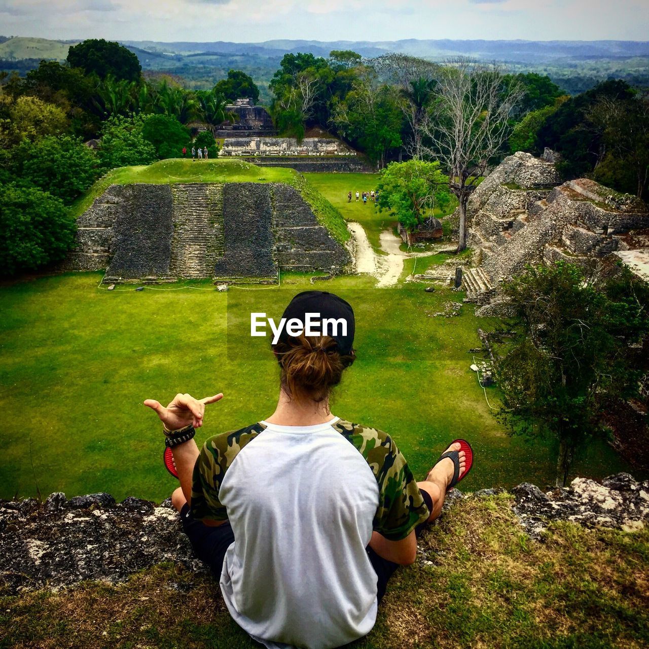 Rear view of man sitting on cliff against old ruins