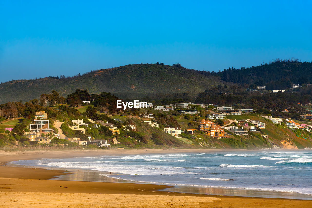 land, body of water, water, beach, sea, shore, coast, sky, scenics - nature, nature, architecture, environment, ocean, travel destinations, mountain, sand, landscape, coastline, beauty in nature, travel, building, vacation, bay, building exterior, wave, tourism, clear sky, tree, no people, built structure, outdoors, blue, sports, motion, plant, city, house, trip, water's edge, tranquility, holiday, sunny, horizon, water sports, summer