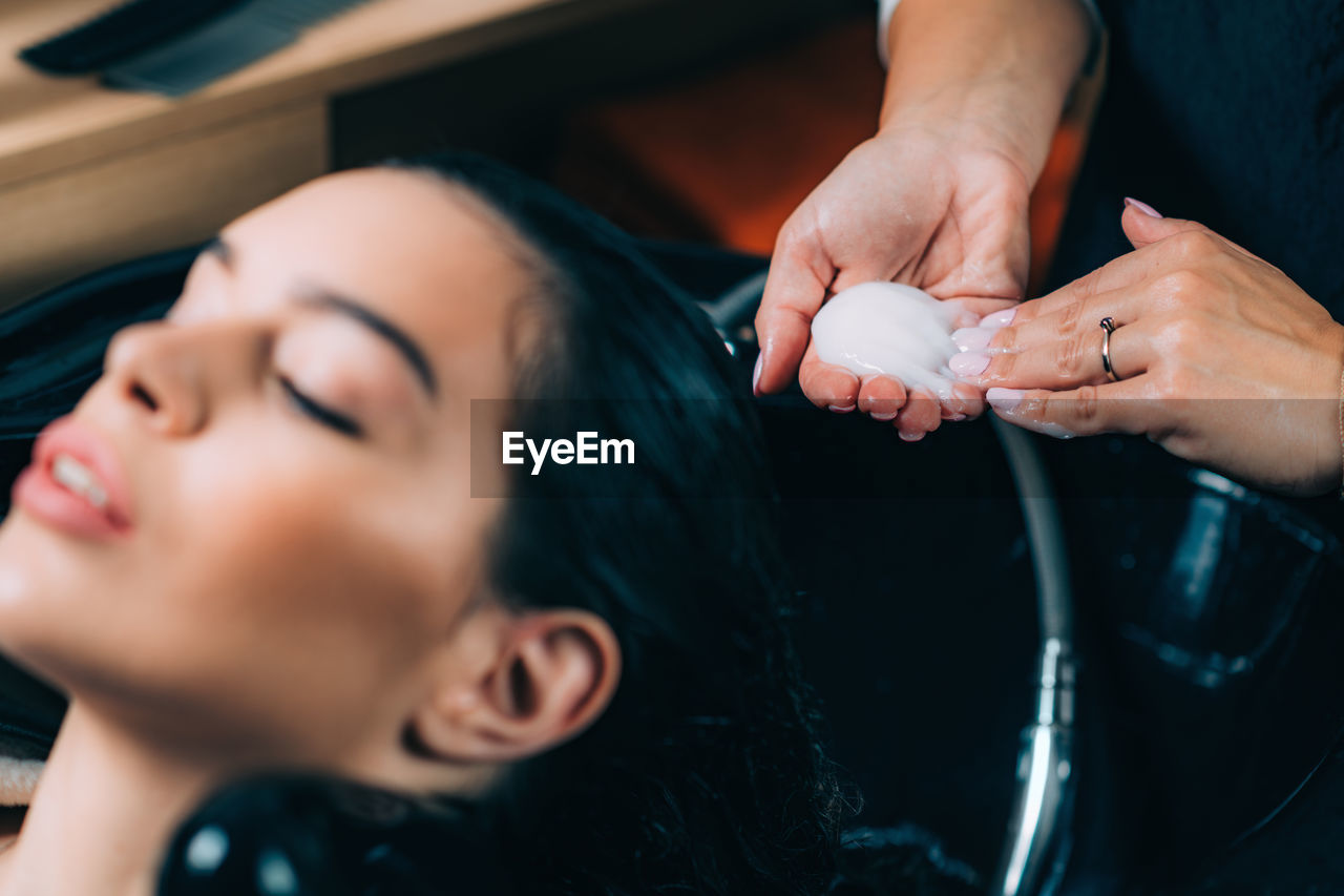 Midsection of hairdresser applying shampoo on woman hair in salon