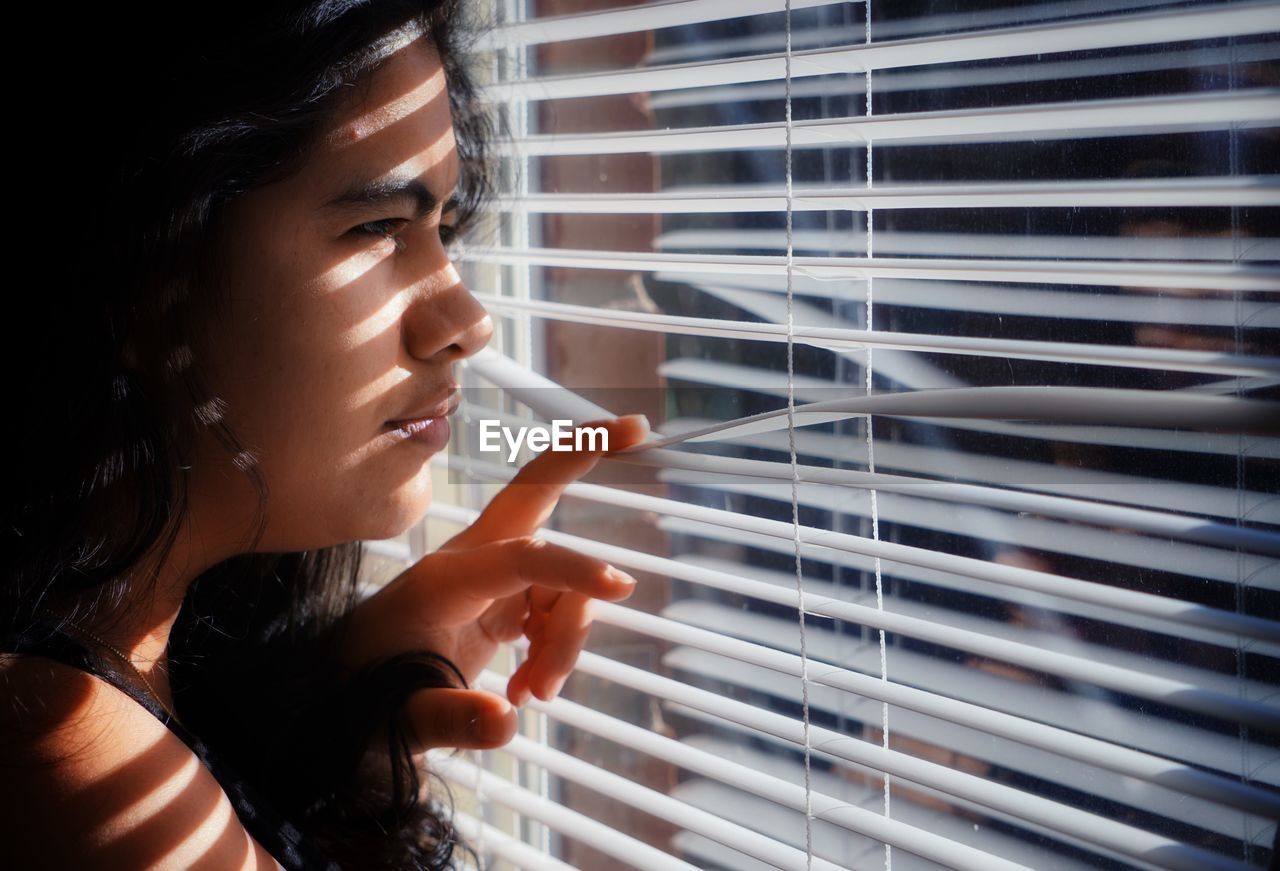 Close-up of woman looking though window blinds