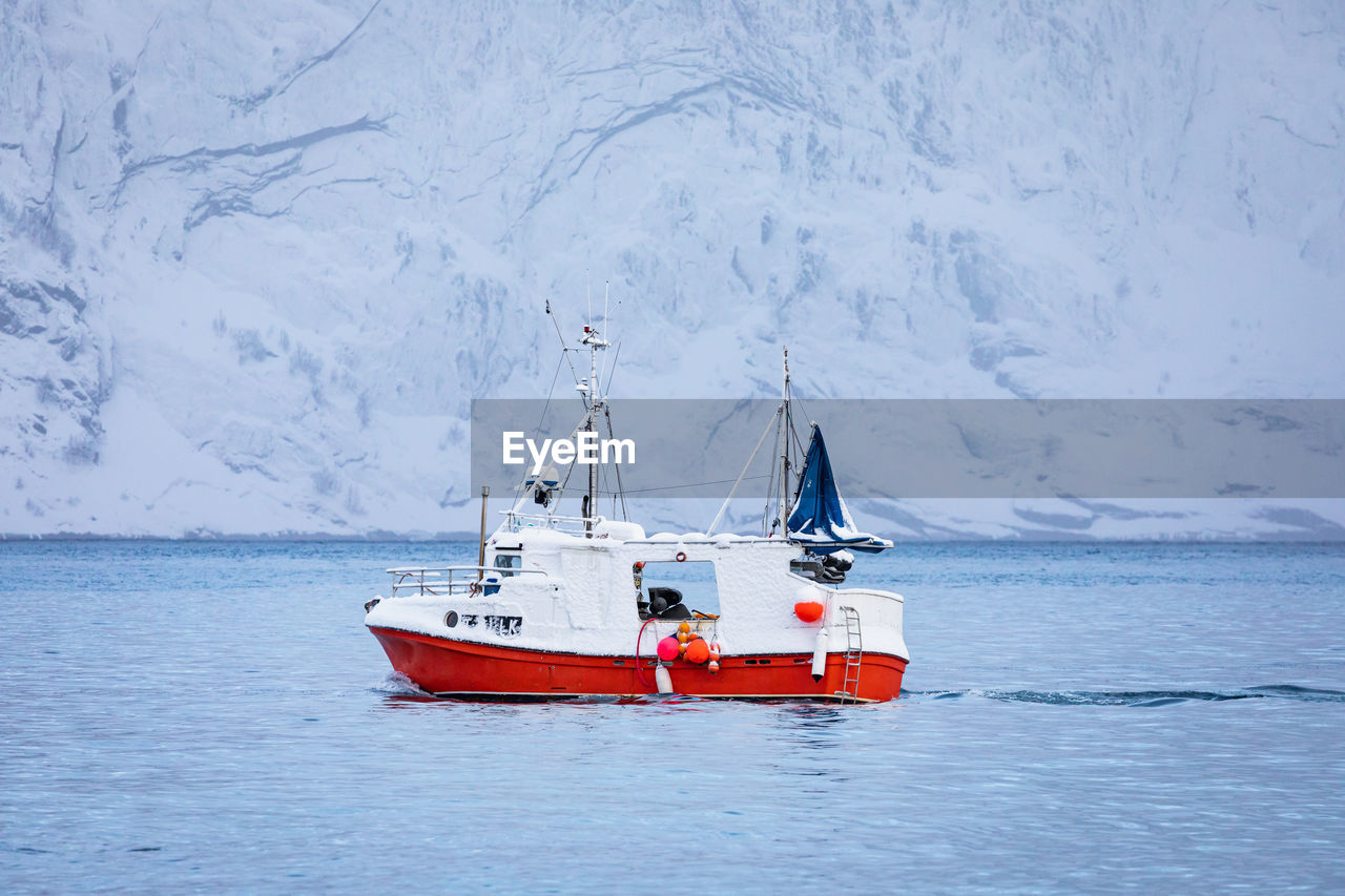 Boat sailing in sea by snowcapped mountain