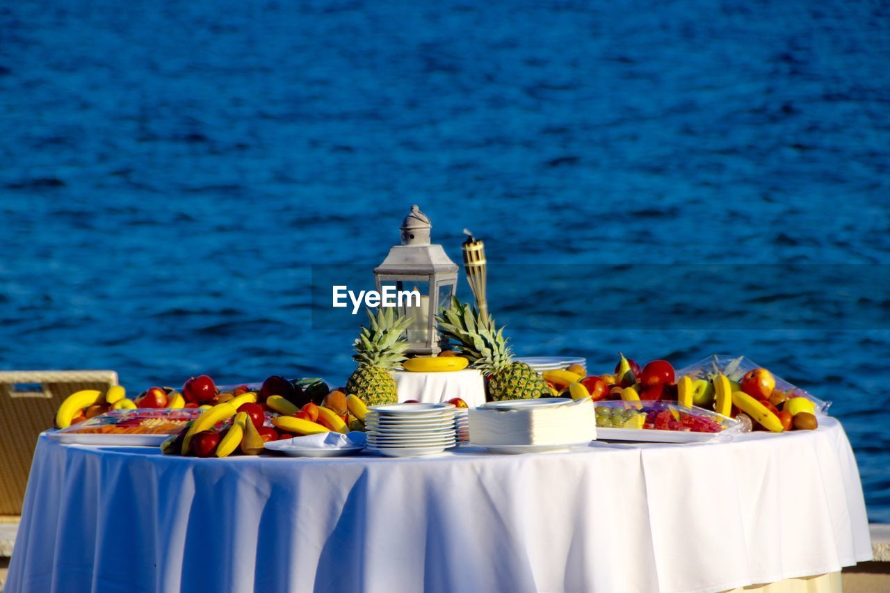 Various fruits on table with lamp against blue water