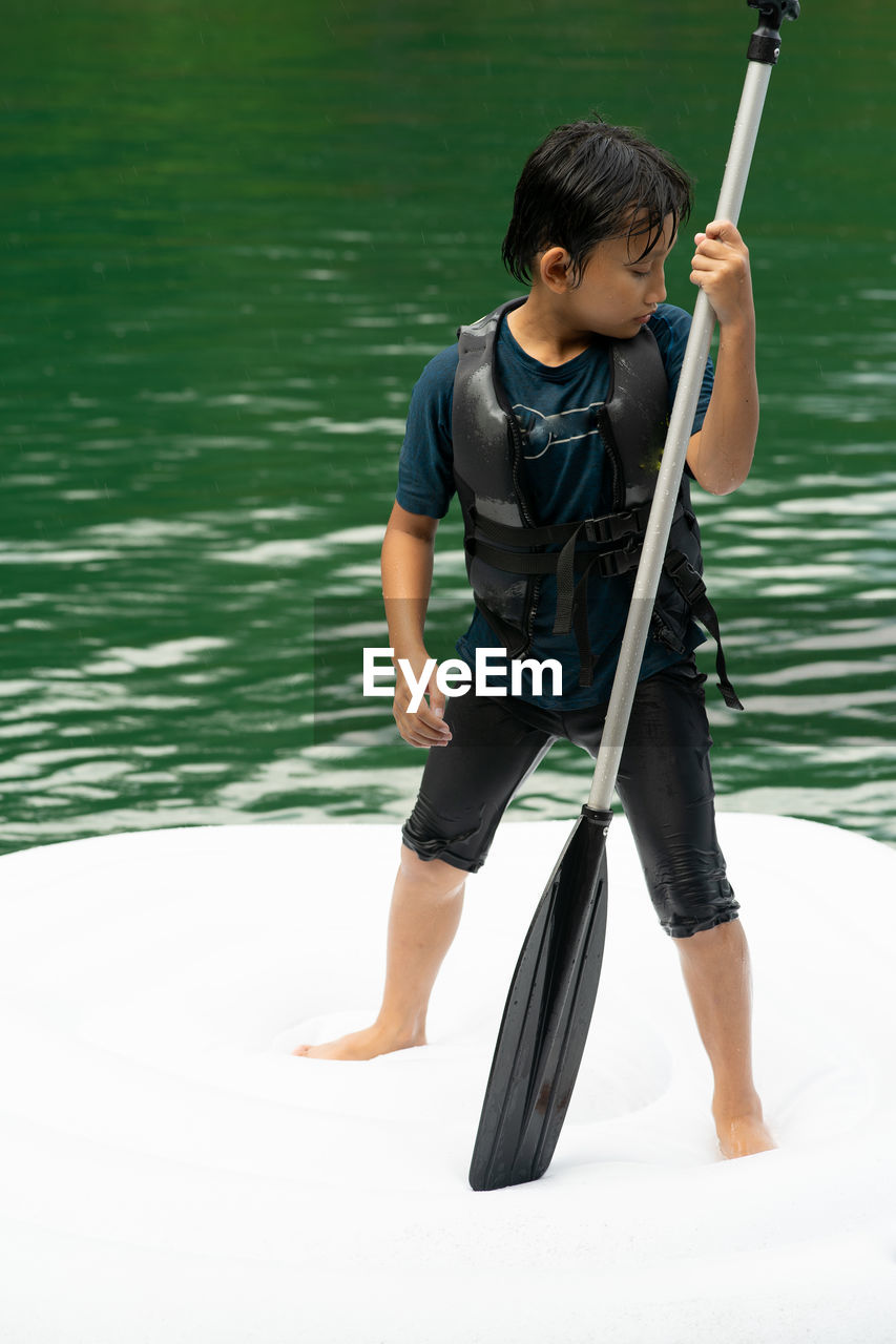 Asian boy wearing life jackets paddling on an inflatable boat in kenyir lake, malaysia.