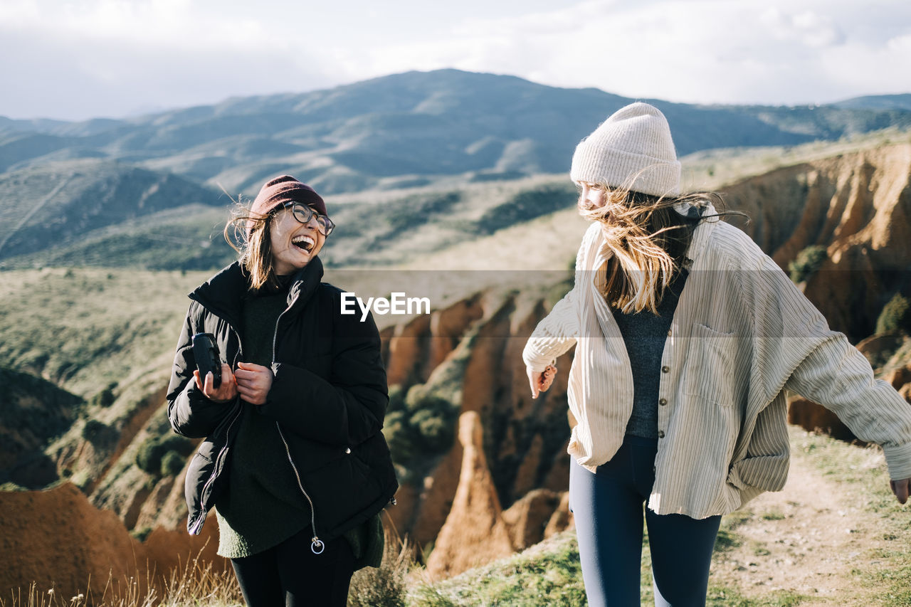 Young happy female travelers with photo camera having fun against mount on sunny day in back lit