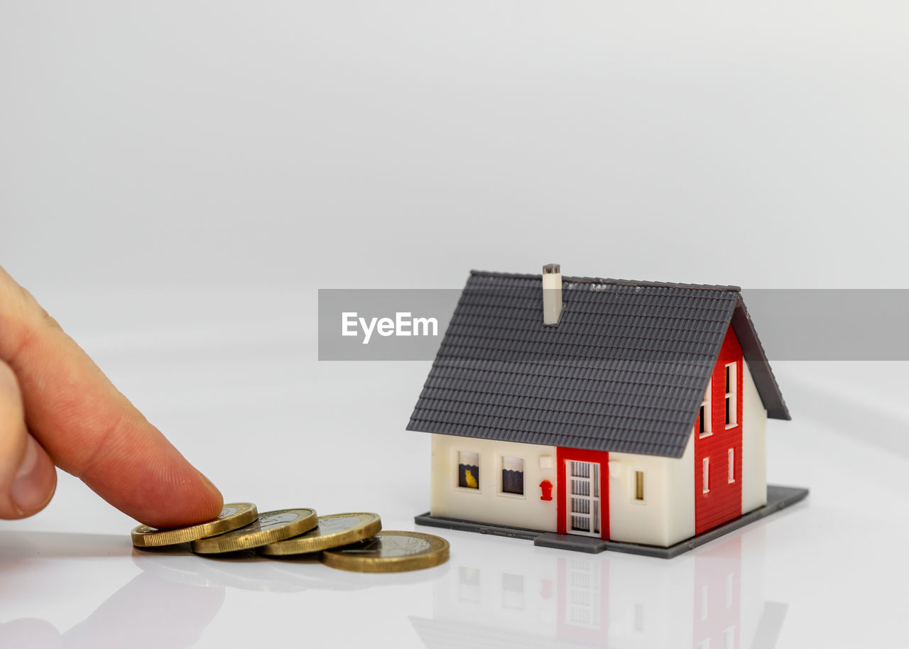 Cropped hand touching coins with model house over white background