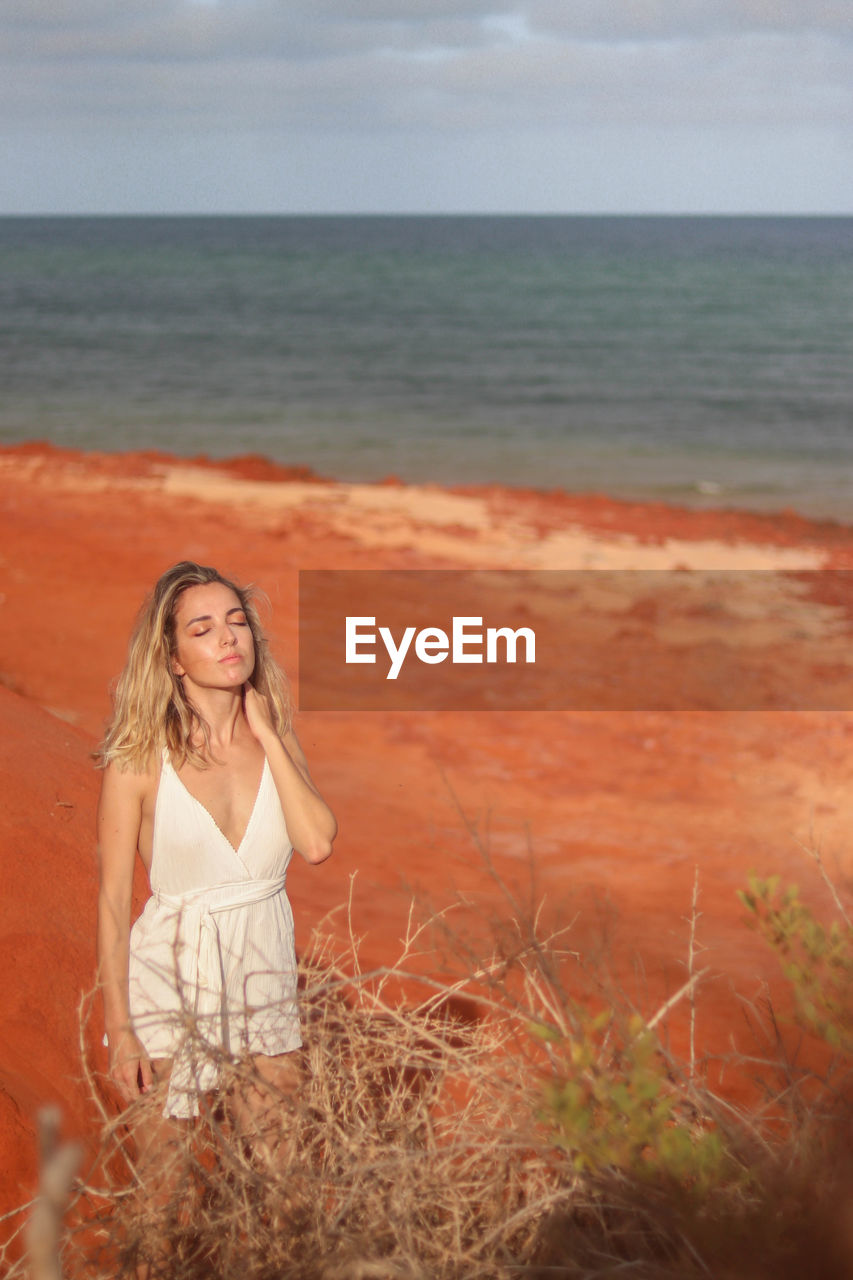 Beautiful young blonde woman in white dress on red sandy beach on the west coast of australia