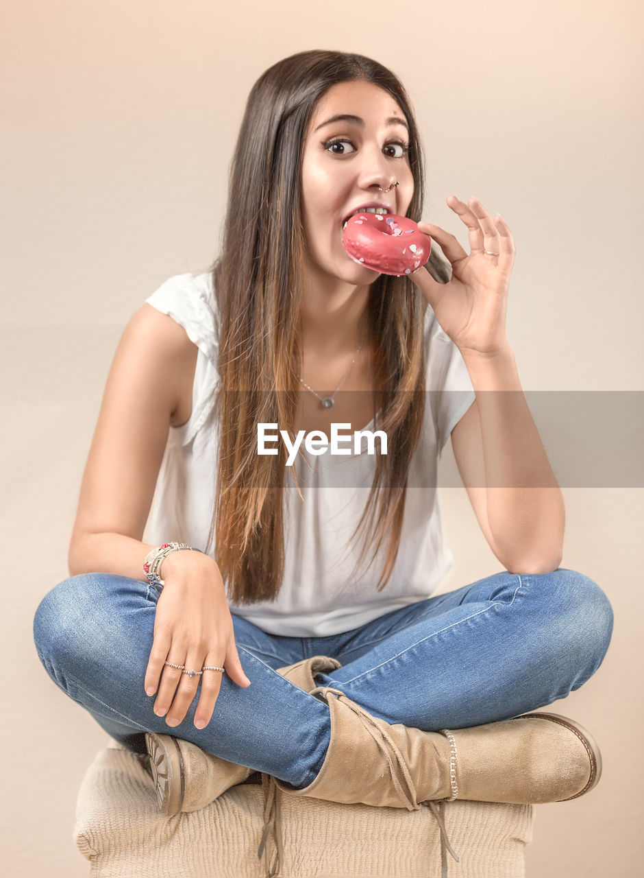 Portrait of young woman eating donut against white background