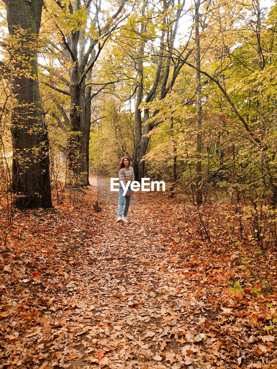 Full length of woman standing amidst leaves in forest