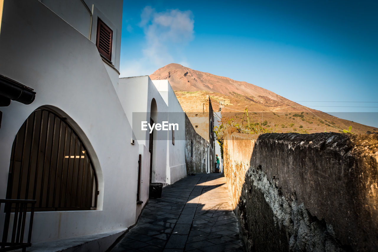 FOOTPATH AMIDST BUILDINGS AGAINST BLUE SKY