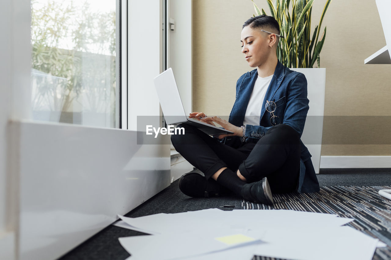 Female professional using laptop while sitting on office floor