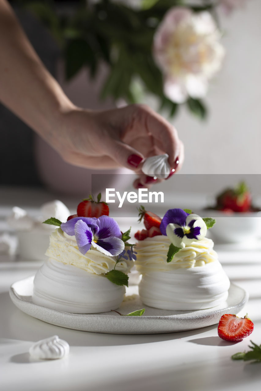 Decorating pavlova's dessert with flowers and berries