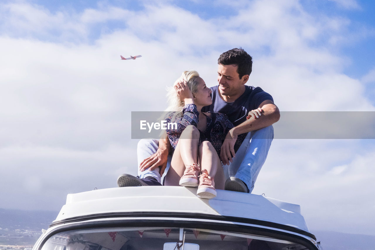 Happy young couple sitting on yacht against sky 
