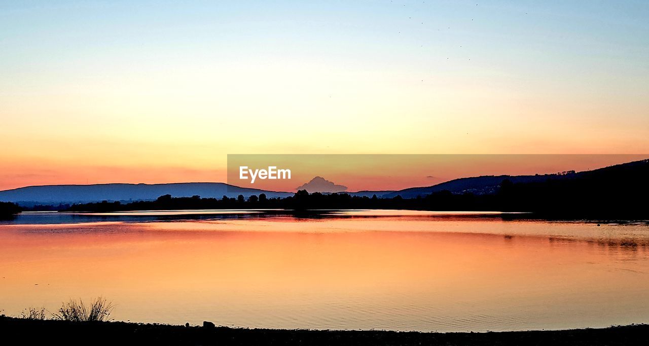 SCENIC VIEW OF LAKE AGAINST SKY AT SUNSET